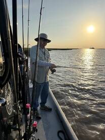 An angler casting a line during a sunset fishing trip, surrounded by fishing rods on a boat.