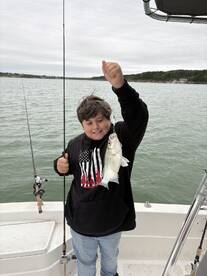 A young angler proudly displaying a freshly caught striped bass while fishing on a boat.