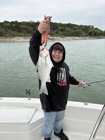 A young angler proudly displaying a large striped bass while fishing on a boat, showcasing the excitement of a successful catch.