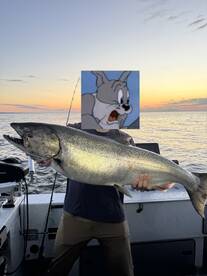 Angler proudly displaying a large fish against a stunning sunset backdrop while fishing on a boat.