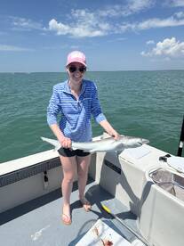 A happy angler proudly displaying a caught shark while fishing on a sunny day.
