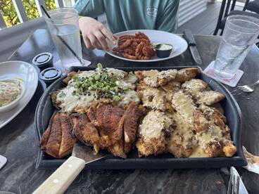 A delicious seafood meal featuring fried fish with toppings, served at a restaurant, with a young person in the background.