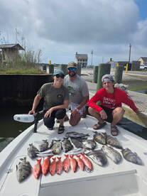 A group of anglers proudly displaying a variety of fish, including Red Snapper and Black Drum, on the deck of a boat after a successful fishing trip.