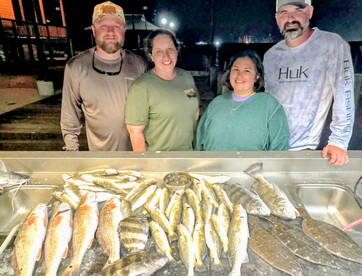 A group of anglers proudly displaying their catch of various fish, including Redfish and Flounder, arranged on a cleaning table after a successful night fishing trip.