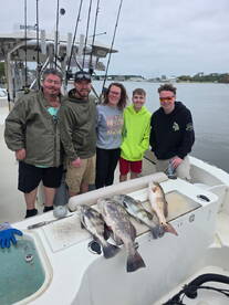 A family group proudly displays their catch of several fish, including black drum and redfish, on the boat after a successful fishing trip.