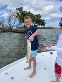 A young angler proudly displaying a Snook while fishing on a boat in a scenic coastal environment.