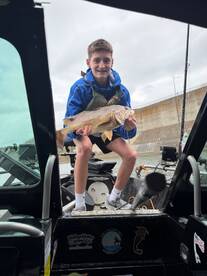 A young angler proudly displaying a large Largemouth Bass while standing in a fishing boat, showcasing a successful day on the water.