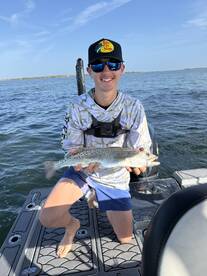 Young angler proudly holding a Speckled Trout while fishing on a boat in a coastal waterway.