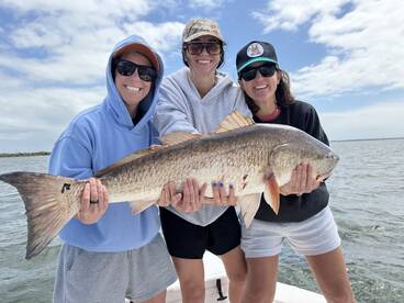 Three anglers proudly displaying a large Redfish while enjoying a day on the water.