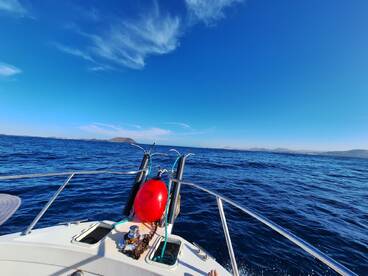 A scenic view from the bow of a boat, showcasing the clear blue waters and distant land, perfect for a day of fishing.