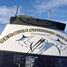 The exterior of the Resacca Fishing Charter boat, showcasing its branding and location in Corralejo, under a clear blue sky.