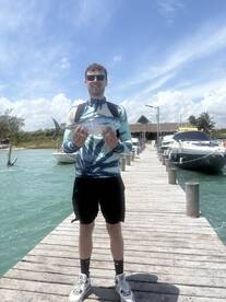 Angler proudly displaying a freshly caught fish on a sunny day at the dock, surrounded by boats.