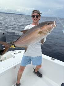 Angler proudly displaying a large Amberjack while fishing on a boat in open waters.