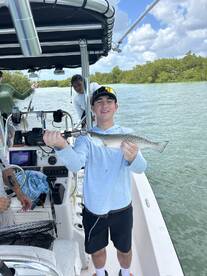 A young angler proudly displaying a Speckled Trout while fishing in a scenic mangrove area.