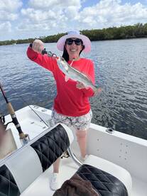 Angler proudly displaying a Speckled Trout while fishing from a boat in a scenic waterway.