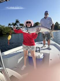 A proud angler holding a large Tarpon on a sunny day while fishing from a boat in a tropical setting.