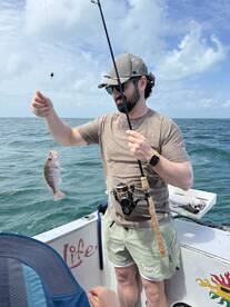An angler reeling in a small Snapper while fishing on a boat in open water, showcasing the excitement of the catch.