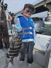 A young angler proudly displaying a large striped bass while fishing from a boat, showcasing a fun day on the water.