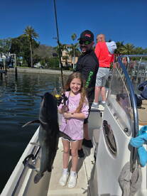 A young girl proudly holding a fish while fishing with family on a sunny day, showcasing a fun and engaging fishing experience.
