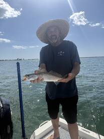 Angler holding a Speckled Trout while fishing on a sunny day, showcasing a successful catch from the boat.