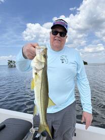 Angler proudly displaying a Snook caught while fishing on a boat, surrounded by a scenic water backdrop.