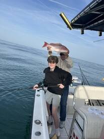 A young angler poses with a large Snapper while an adult holds it up, showcasing their successful catch on a fishing trip.