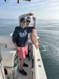 Two anglers proudly displaying a large Red Snapper while fishing on a boat in calm waters.
