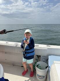 A young angler proudly holding a fish while fishing on a boat, showcasing a fun family fishing experience.