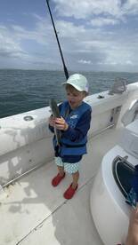 A young angler excitedly holds a small fish while fishing on a boat, showcasing a joyful moment on the water.