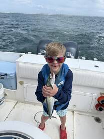 A young angler proudly displaying a Spanish Mackerel while enjoying a fishing trip on a boat.