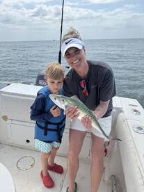 A young boy and his mother proudly display a caught fish while enjoying a day of fishing on the boat.
