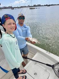 A young angler and a guide proudly displaying a caught fish while fishing from a boat in a coastal area.