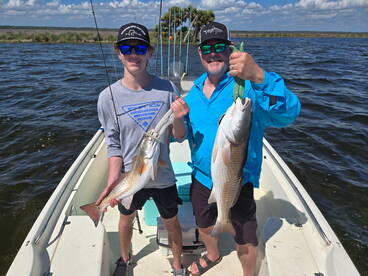 A young angler and an adult proudly displaying their catches of Redfish while fishing on a sunny day.