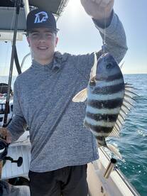 A young angler proudly displaying a Sheepshead caught while fishing on a boat, showcasing a sunny day on the water.