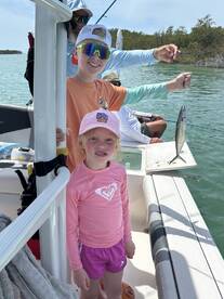 Two young anglers proudly displaying their catch while fishing on a boat in a scenic coastal environment.