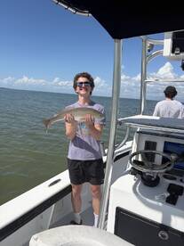 A young angler proudly displaying a Redfish while fishing on a boat in sunny weather.