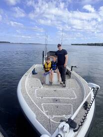 A family enjoying a day on a fishing boat, with two young boys wearing life jackets and a parent posing with them on the water.