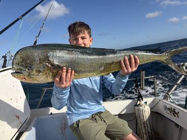 Young angler proudly holding a large Mahi Mahi on a fishing boat, showcasing a successful catch during a deep-sea fishing trip.