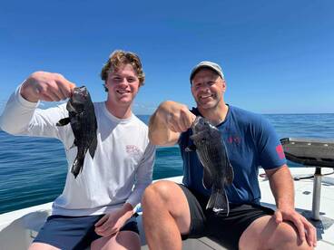 A young angler and an adult proudly displaying their Black Sea Bass catch while enjoying a sunny day on the water.