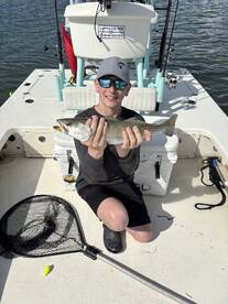 Young angler proudly holding a Speckled Trout on a fishing boat, showcasing a successful day on the water.