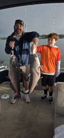 A proud angler and a young boy display their impressive catch of two large Catfish while fishing on a boat.