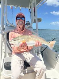 Angler proudly displaying a large Redfish while seated on a boat, enjoying a sunny day on the water.