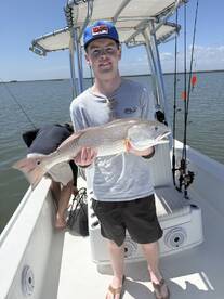 A young angler proudly holding a Redfish while fishing on a boat in a coastal waterway.