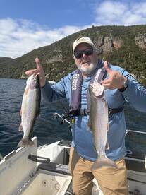 Angler proudly displaying two Rainbow Trout while fishing on a scenic lake, surrounded by lush greenery.