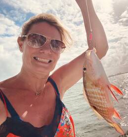 A smiling angler proudly displaying a colorful Snapper while fishing in a sunny coastal environment.