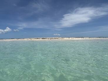 A scenic view of clear turquoise waters and a sandy beach under a blue sky, ideal for fishing or relaxation.