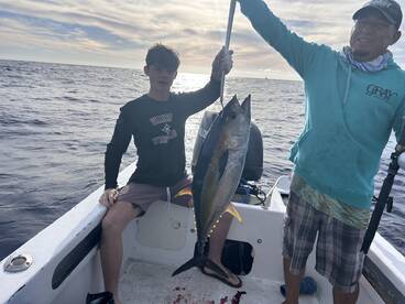 A young angler and a guide proudly display a large Yellowfin Tuna aboard a fishing boat, showcasing a successful deep-sea fishing trip.