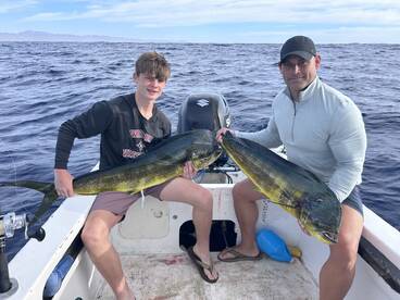 A young angler and an adult proudly displaying their catch of two Mahi Mahi while fishing in open waters.