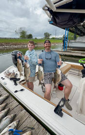 A young angler and an adult proudly displaying their catch of striped bass on a boat after a successful fishing trip.