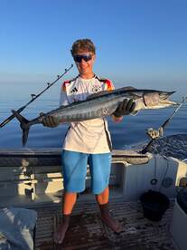 Young angler proudly holding a large Wahoo on a fishing charter, showcasing a successful day on the water.
